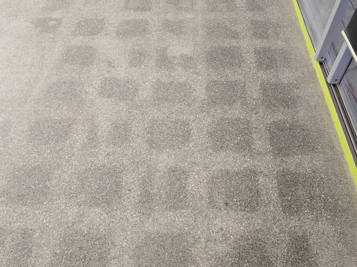 Regular grid of darker squares across a ground concrete floor, left by the adhesive under lifted tiles