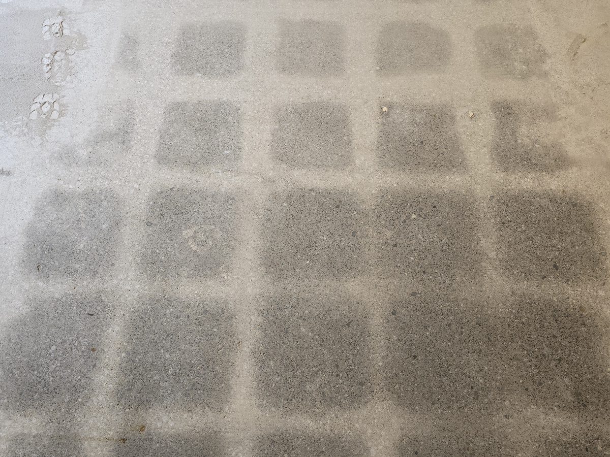 Close view of a ground concrete floor where grinding has made a checkerboard adhesive pattern more clearly visible