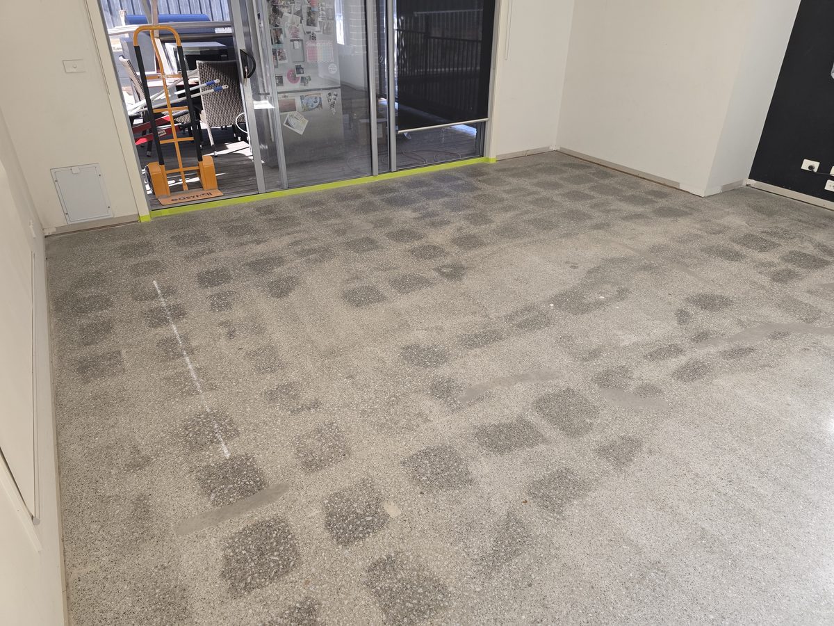 Checkerboard ghosting across a ground concrete floor, where old tile adhesive has left a grid of darker squares