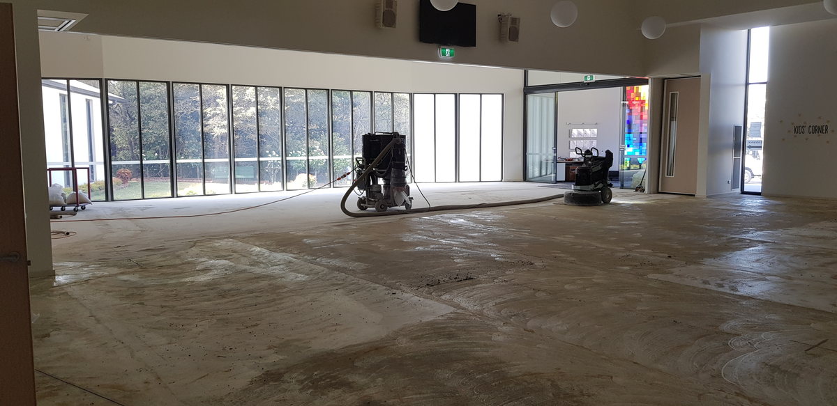 Two industrial concrete grinders with dust extraction preparing a large hall floor