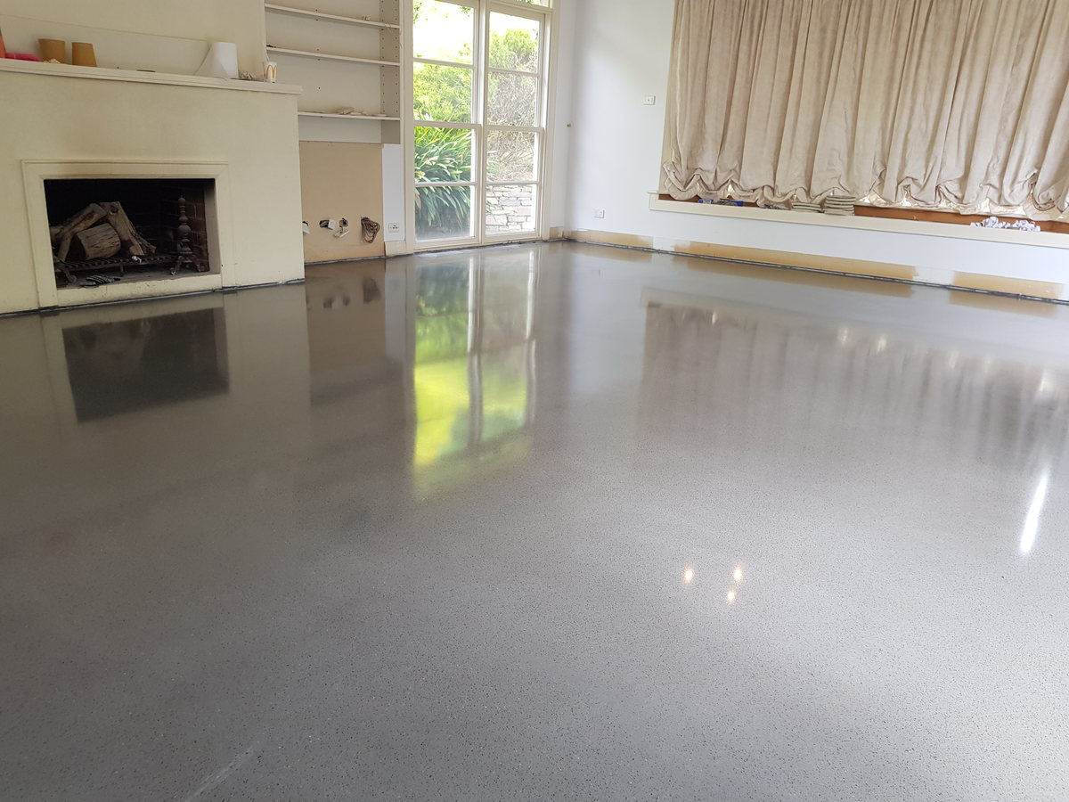 Highly reflective decorative concrete overlay in a large room with a fireplace and curtains