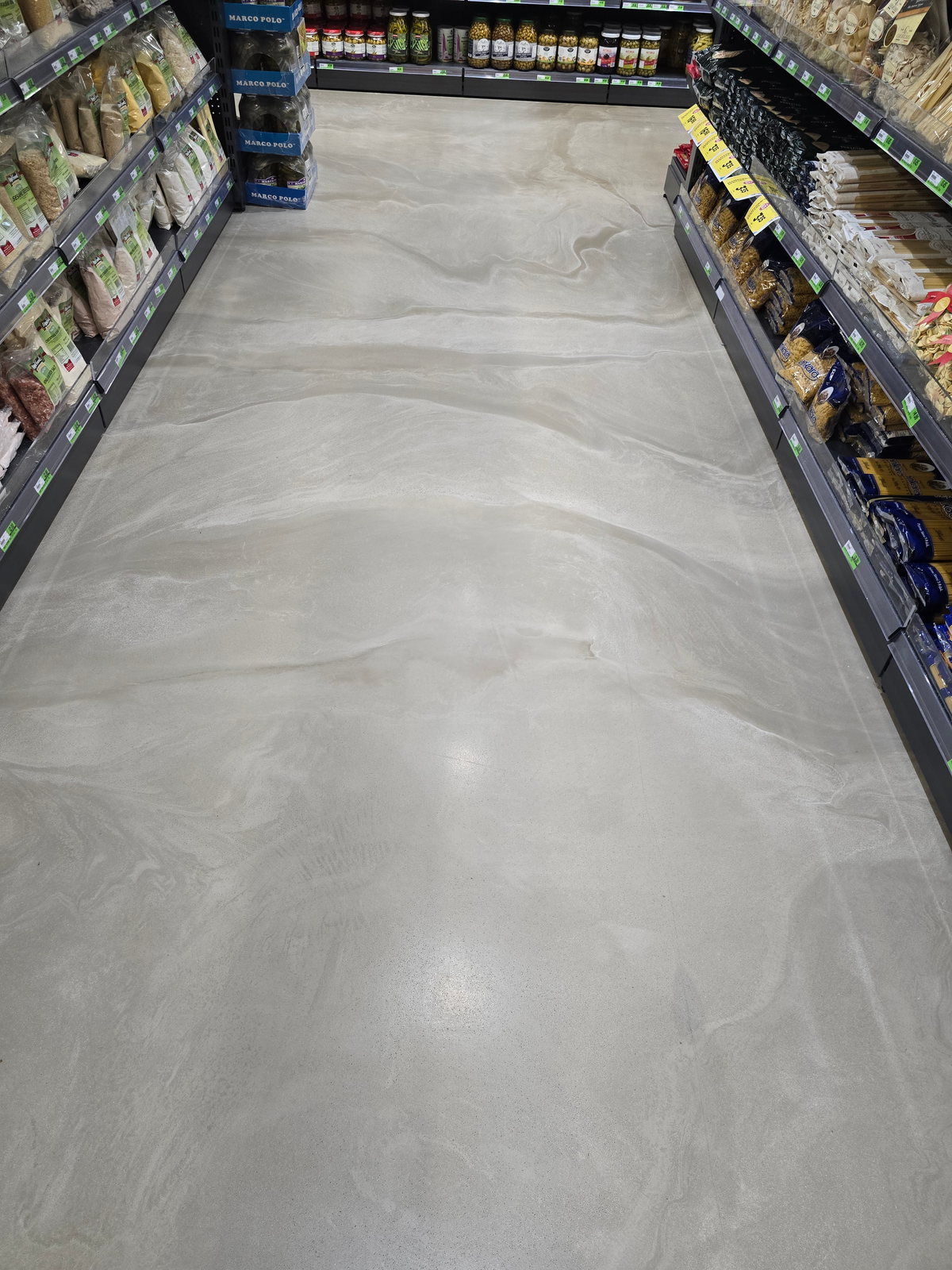 Decorative concrete overlay floor running the length of a stocked supermarket aisle