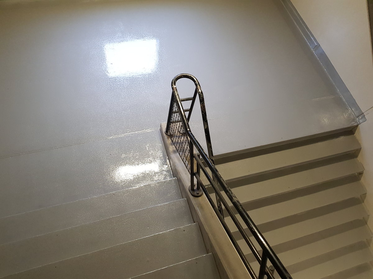 Cream epoxy stair coating with a metal handrail in a stairwell