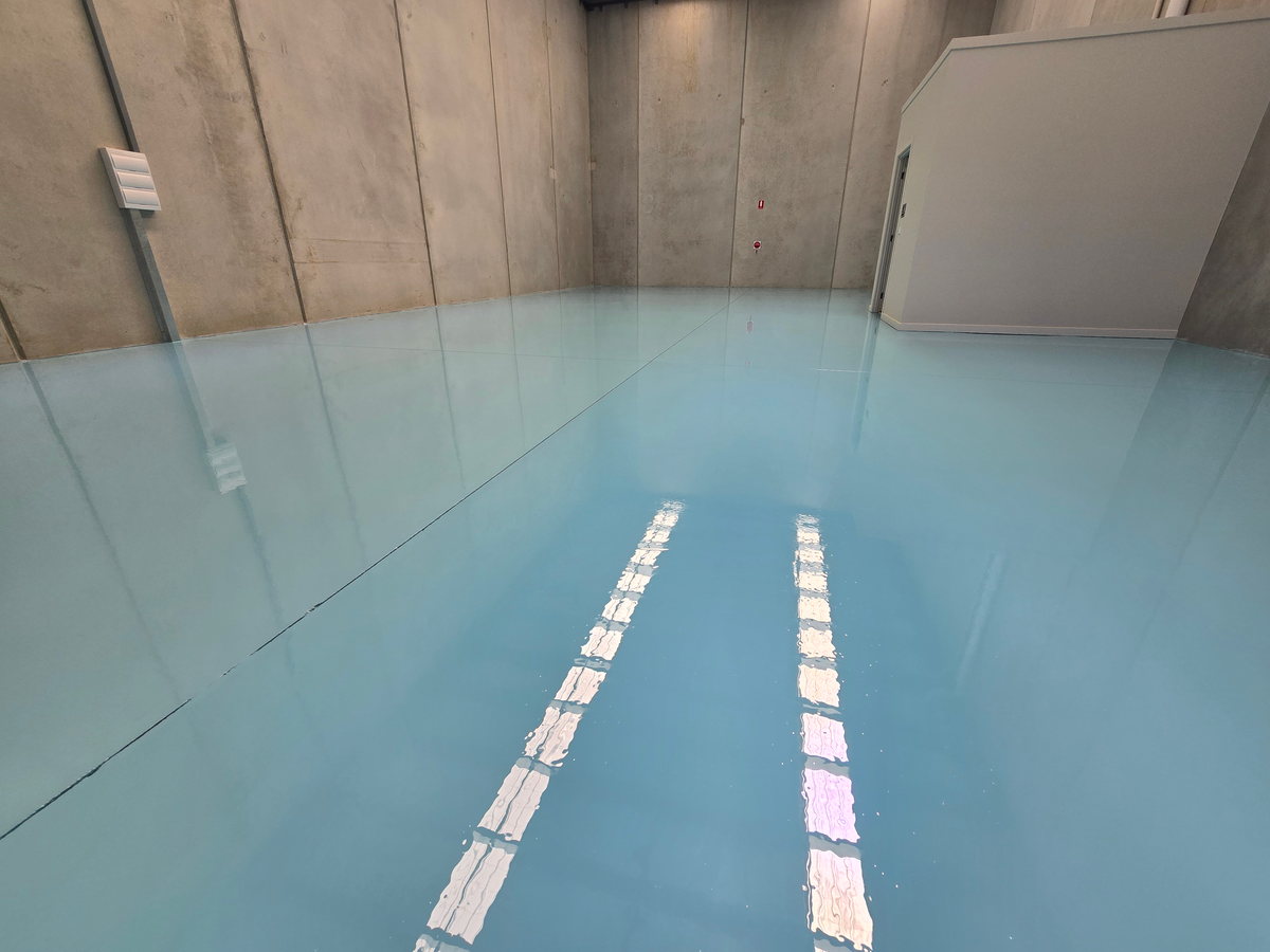 Blue epoxy warehouse floor with white safety line markings between concrete walls