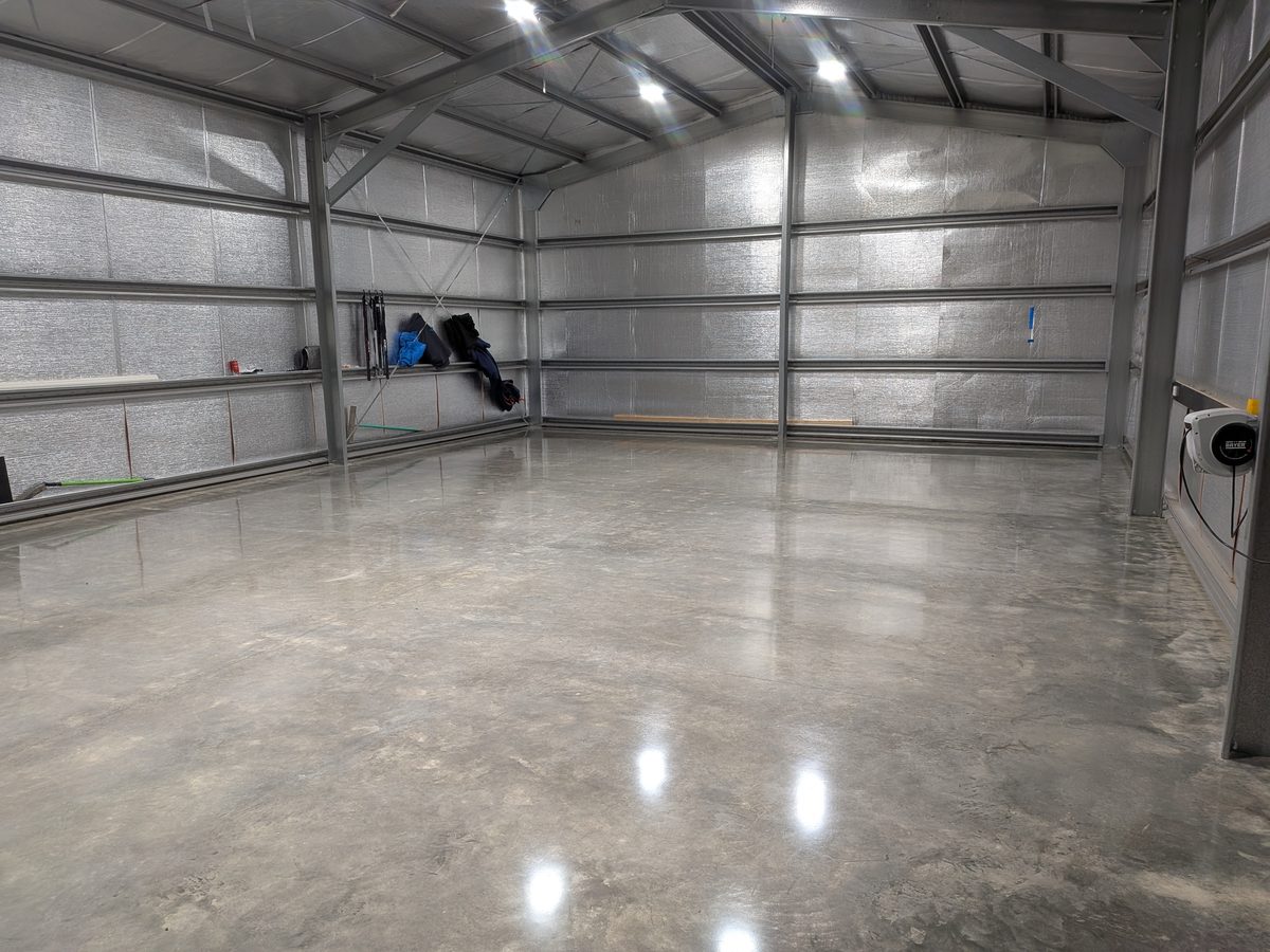 Factory-spec polished concrete floor across a wide empty steel shed, reflecting the roof lights in a clean unbroken surface