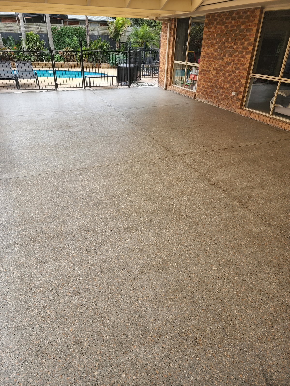 Honed and sealed concrete patio beside a fenced swimming pool at a brick house