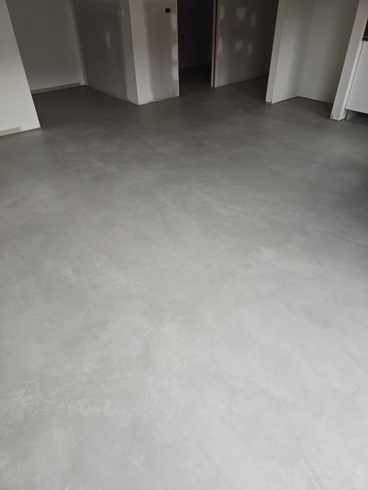 Grey microcement floor with visible hand-trowelled sweep marks running seamlessly through a room and into adjoining doorways