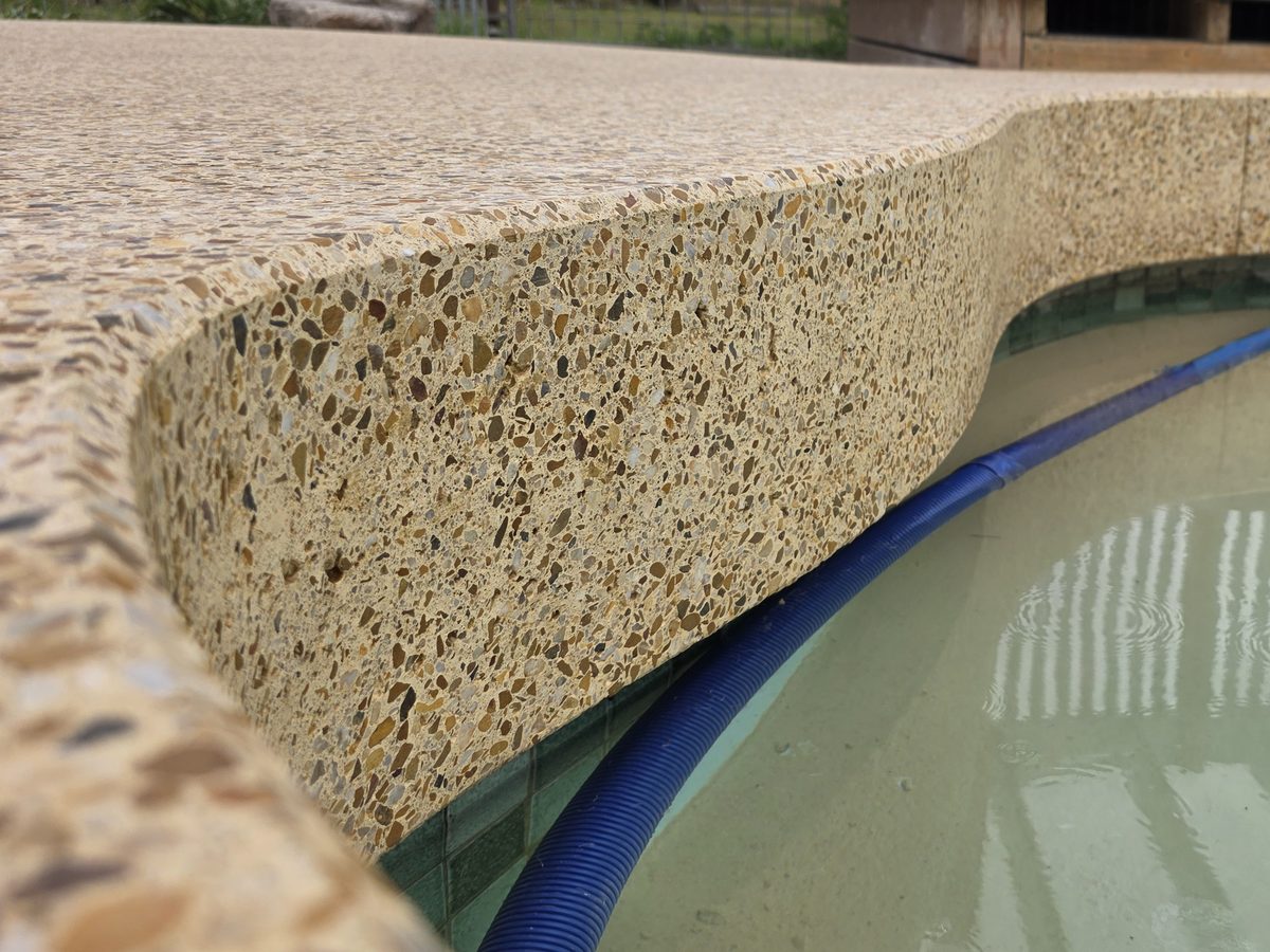 Cross-section of a finished pavilion pool coping, the ground edge showing multicoloured stone aggregate exposed through the surface