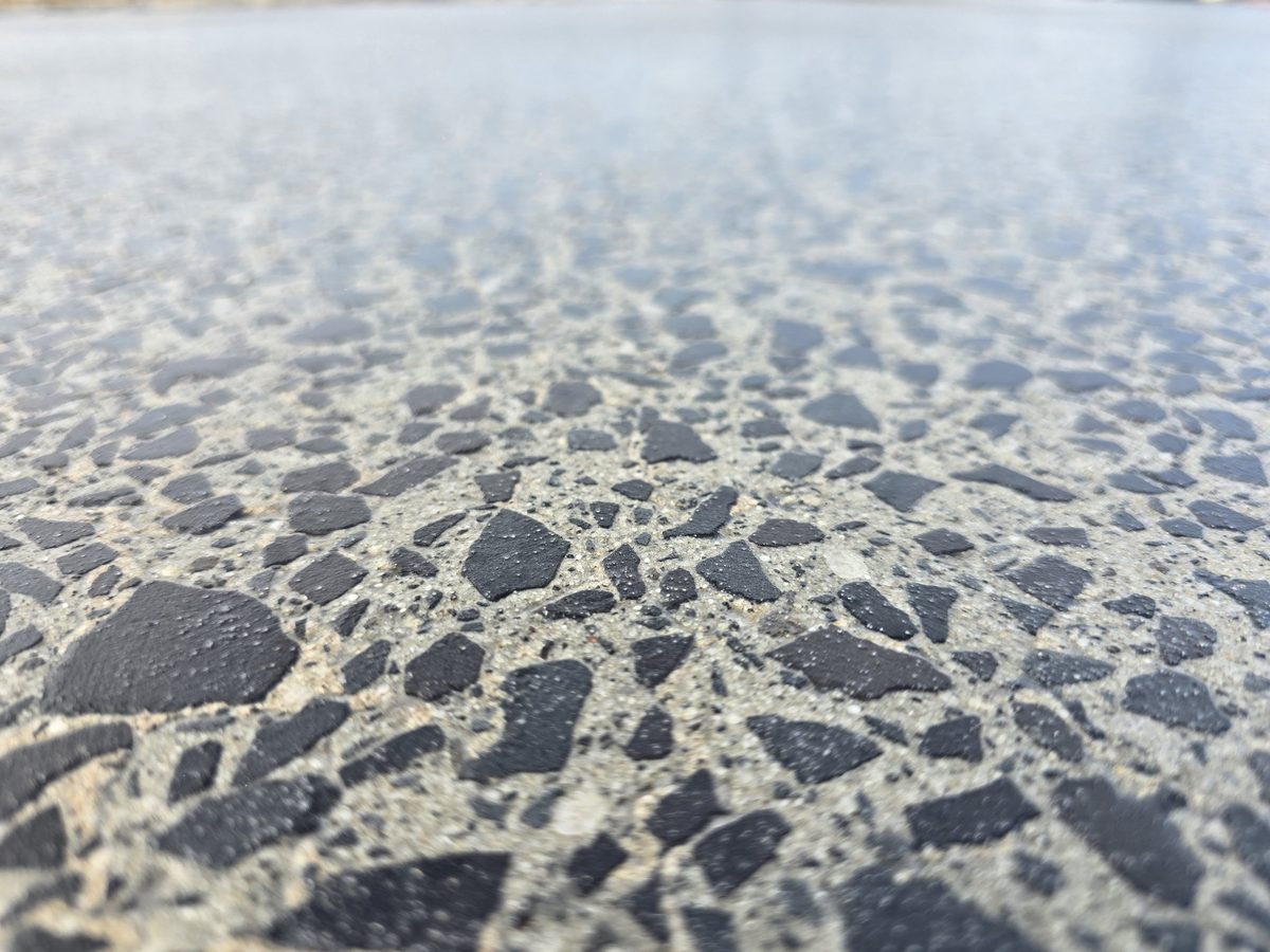 Close-up of a pavilion finish showing dark stone aggregate exposed in a textured outdoor surface