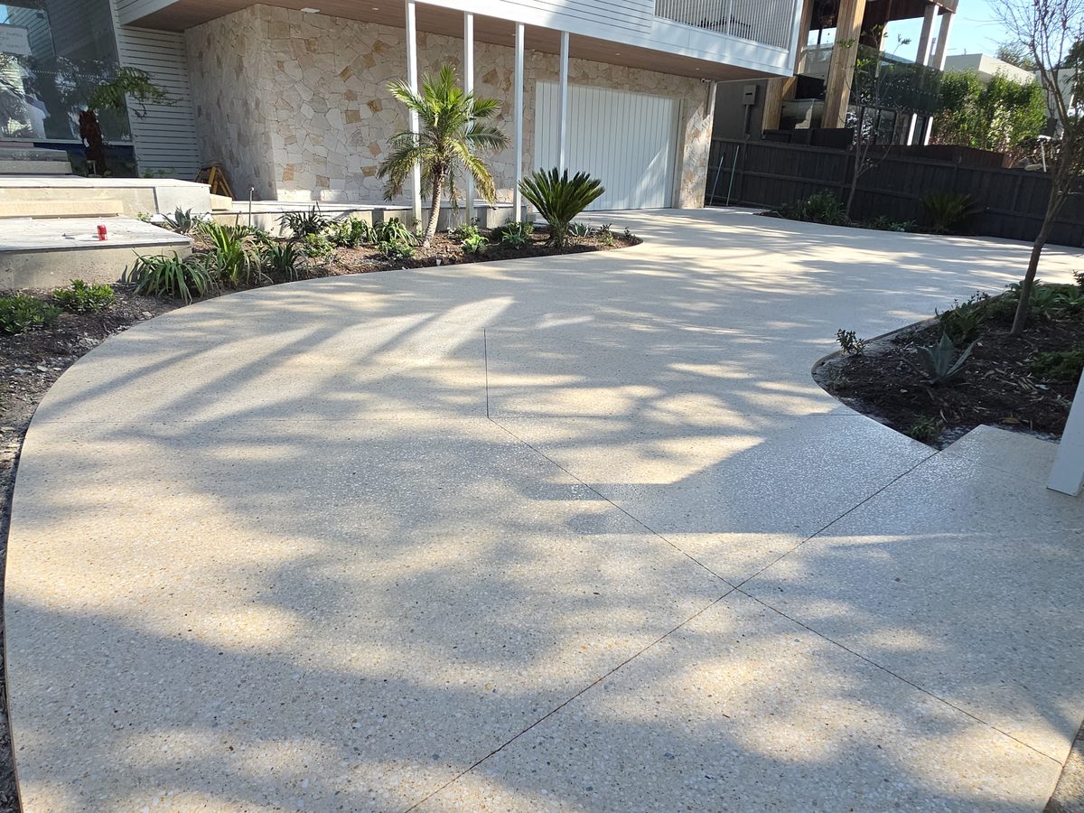 Exposed-aggregate pavilion finish driveway sweeping to a house entry past established palms