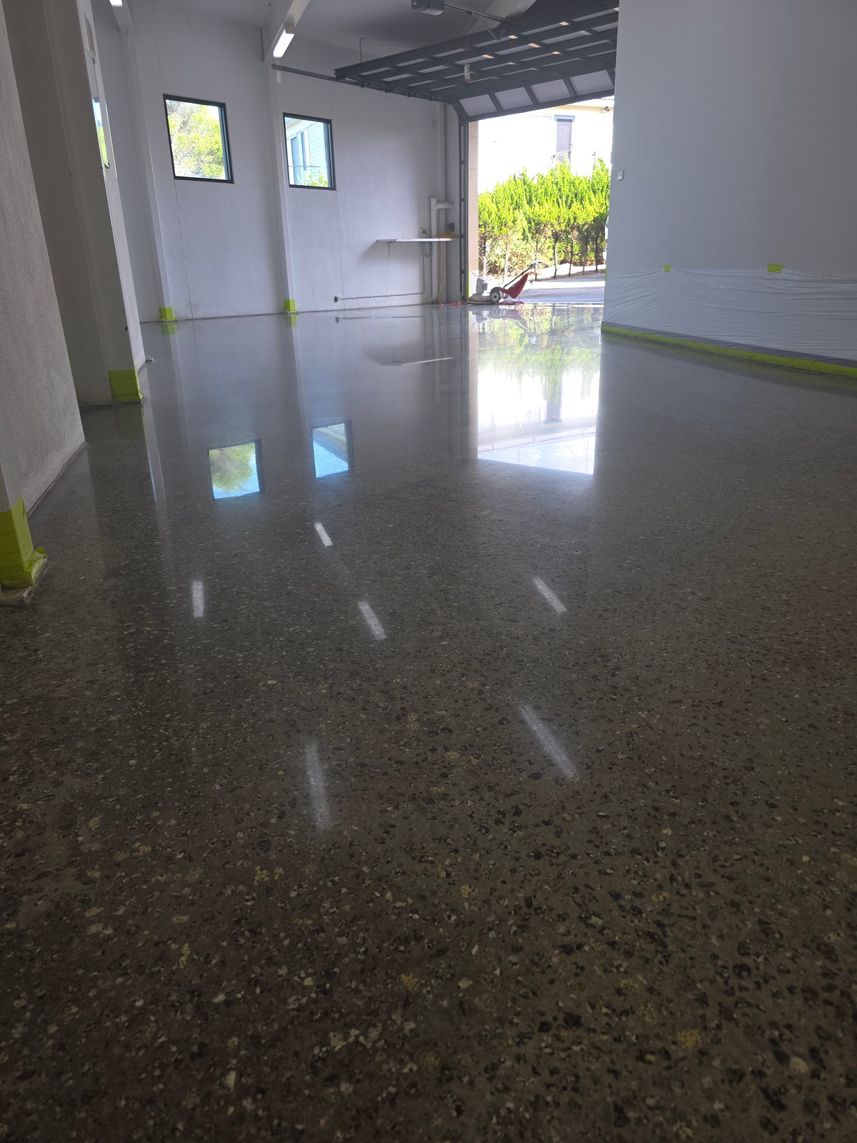 High-gloss charcoal polished concrete floor with dense exposed aggregate reflecting daylight from an open garden doorway