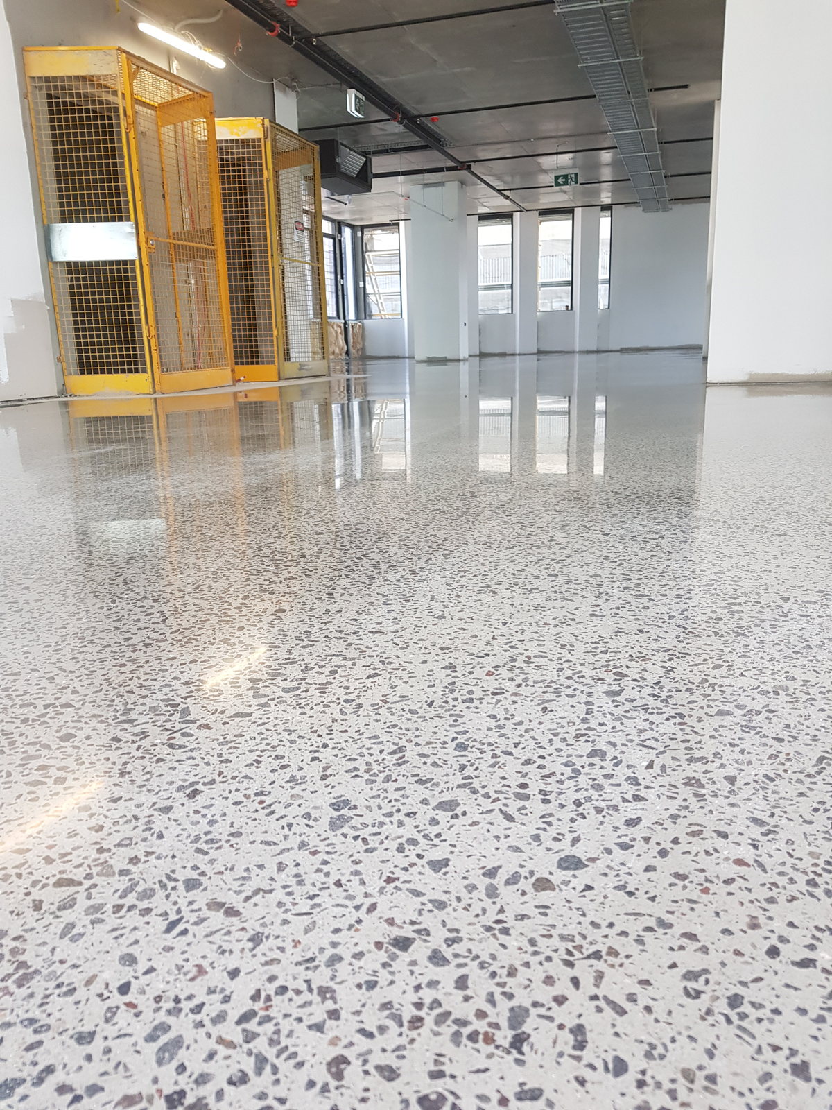 Commercial polished concrete floor with dense salt-and-pepper aggregate beside a glazed partition