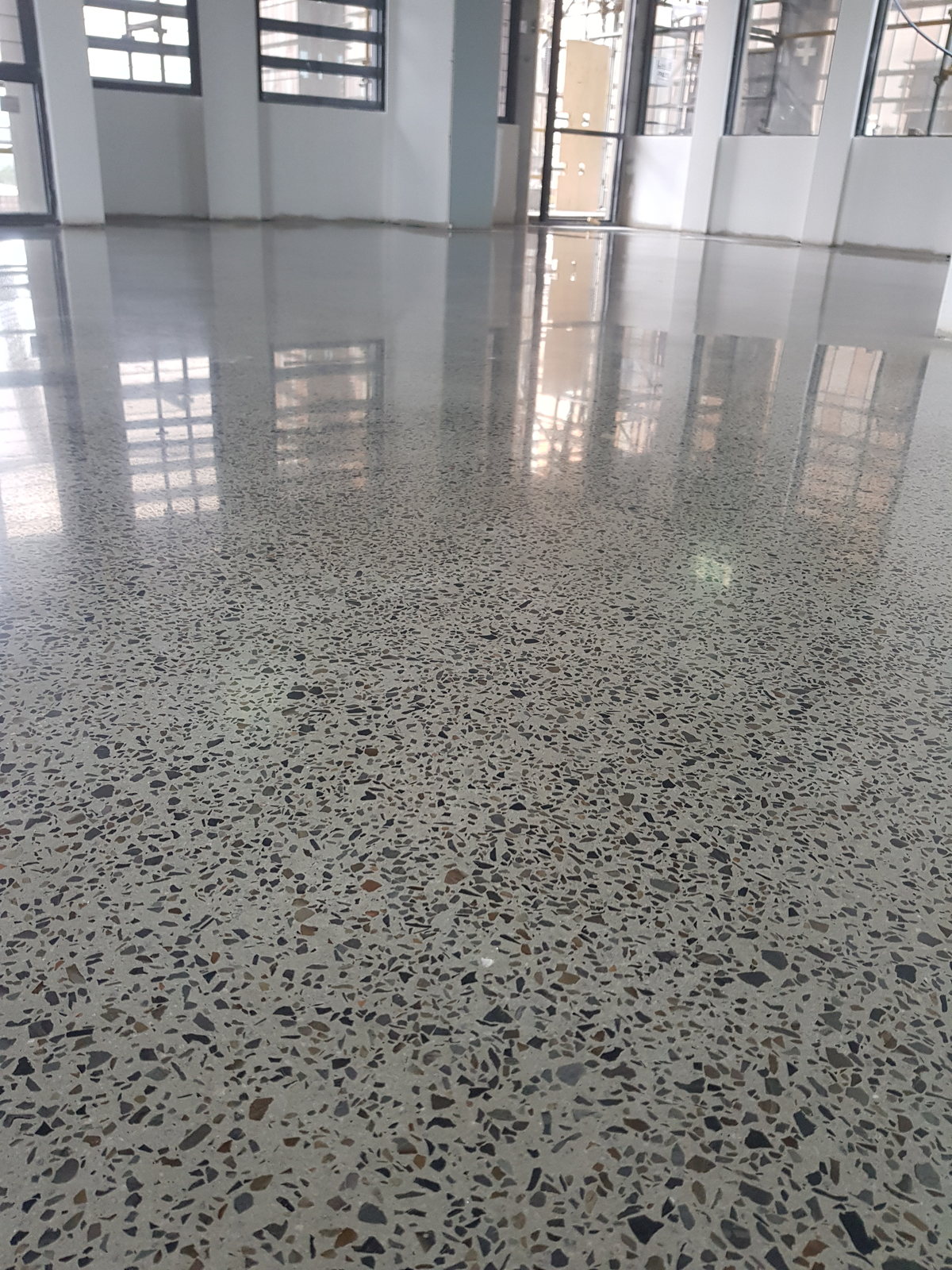 Polished concrete floor with dark exposed aggregate reflecting a wall of office windows