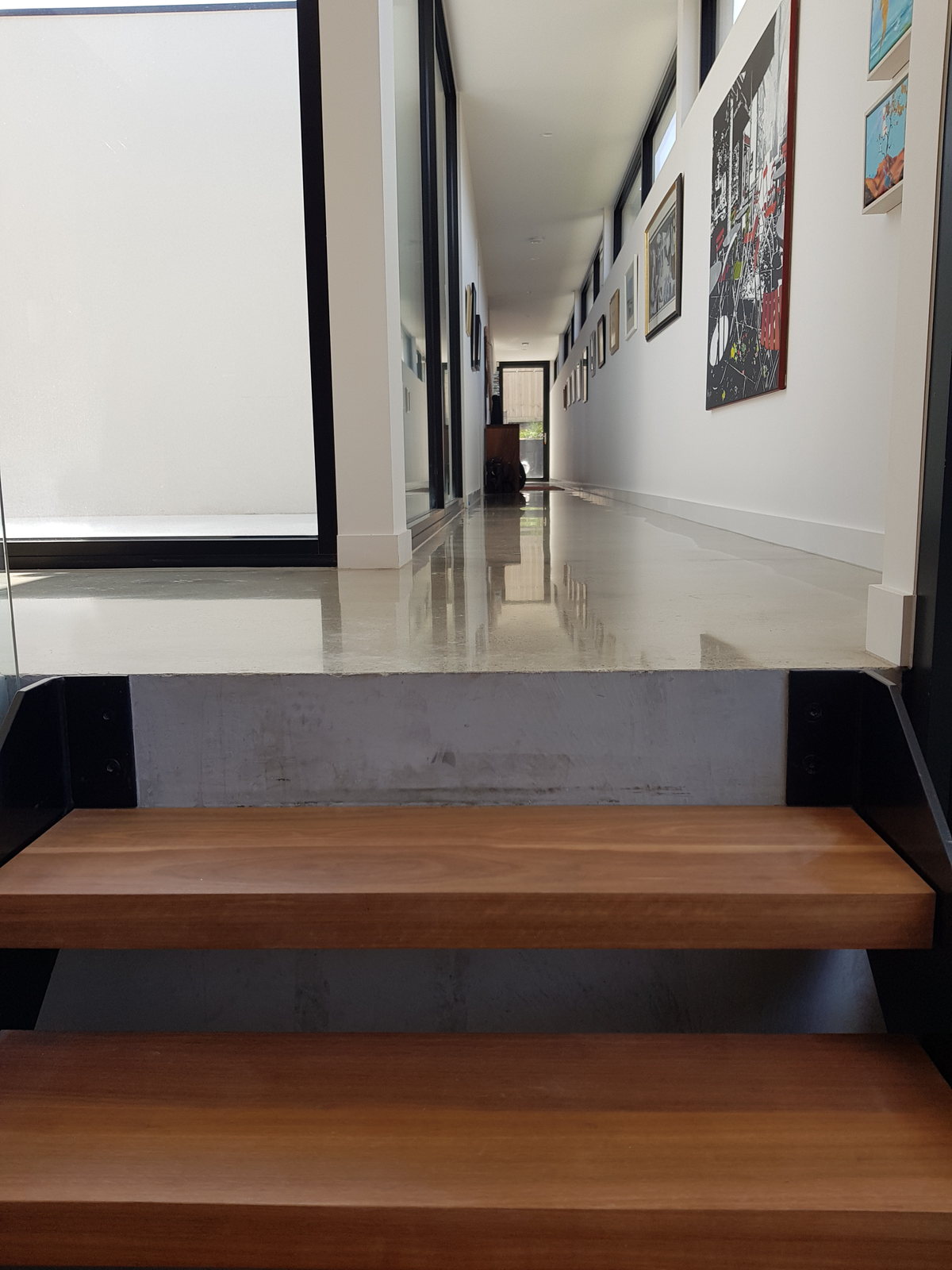 Floating timber stair treads rising from a polished concrete floor in a white hallway