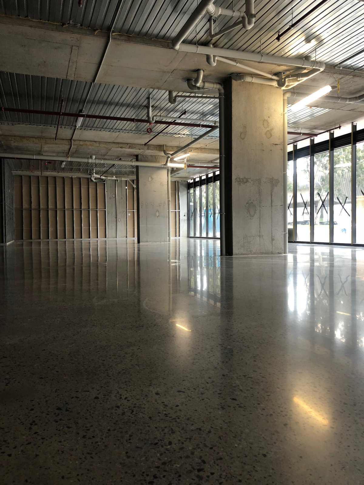 Polished concrete floor in a retail tenancy with a concrete column and exposed ceiling services